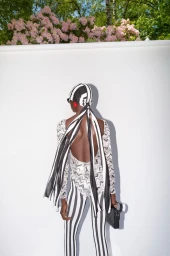 Model from behind wearing a black and white patterned headscarf and striped trousers against a plain white backdrop