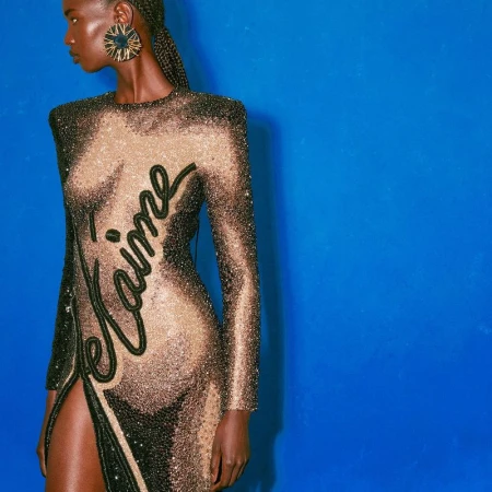 Elegant woman in a long shimmering gown with 'Je t'aime' text poses against a vibrant blue backdrop, showcasing fashion and style.