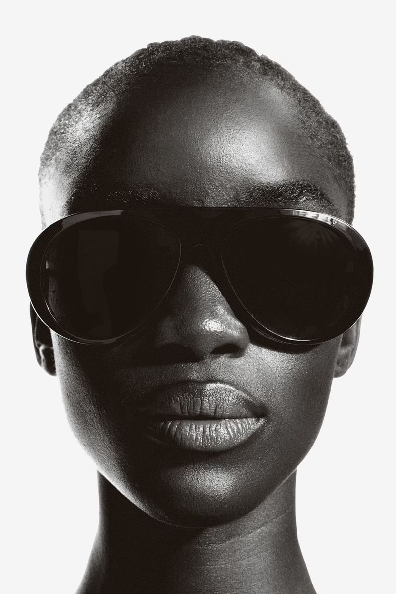 Close-up studio shot of an adult African American female model wearing aviator sunglasses against a bright white backdrop.