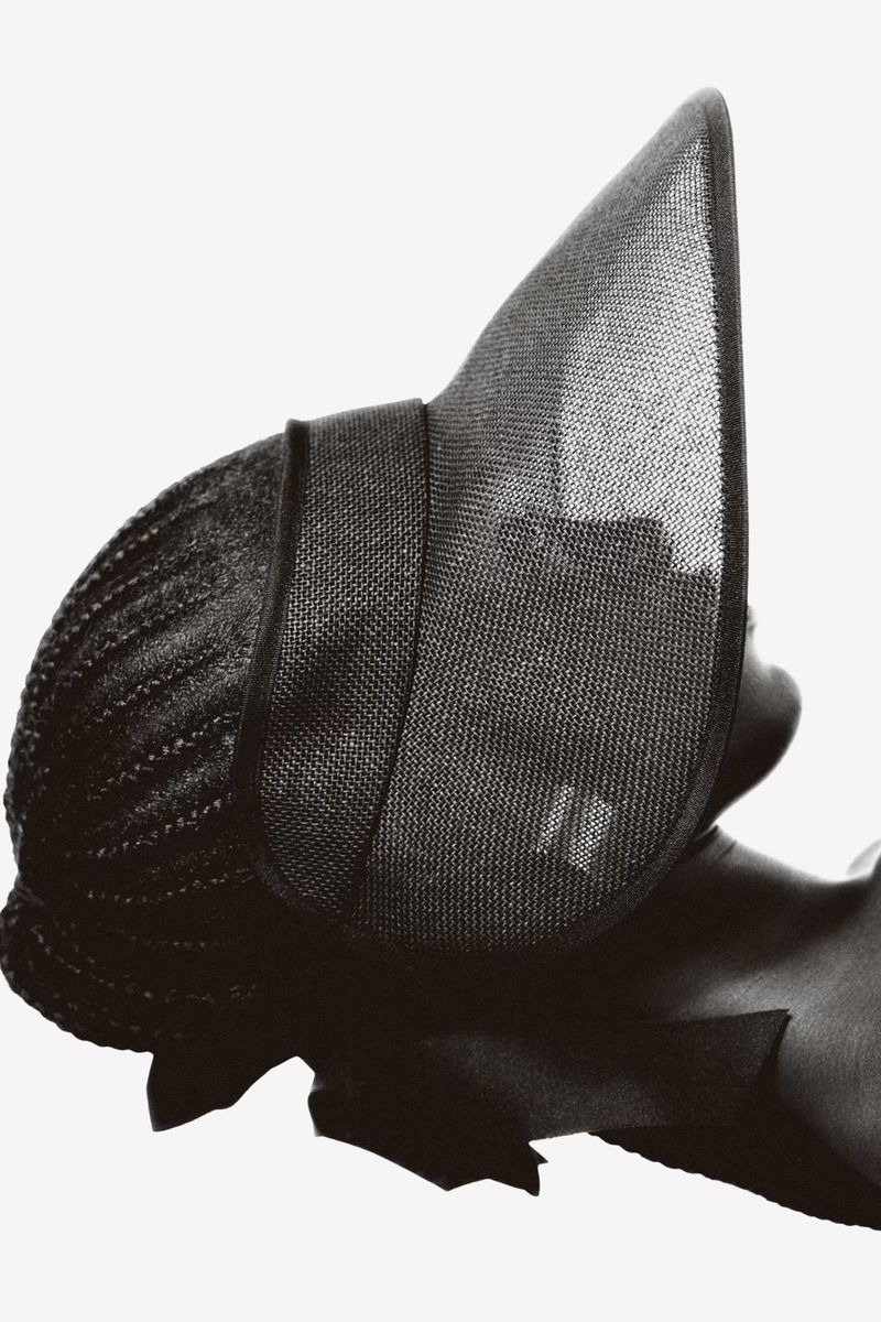 Headshot of a woman wearing an elaborate dark sun hat against a white background, high-fashion, beauty shot, studio lighting.
