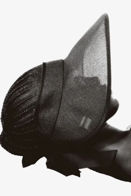 Headshot of a woman wearing an elaborate dark sun hat against a white background, high-fashion, beauty shot, studio lighting.