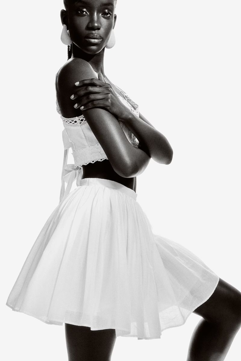 Monochrome fashion portrait of a black woman wearing a white cotton top and skirt with arms crossed in a photo studio setting.