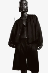 Model Maty Fall wearing black blouse and shorts against a white background for H and M lookbook