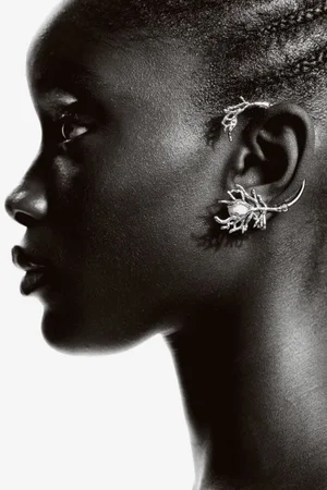 Close-up profile of model Maty Fall wearing sculptural silver ear cuffs against a seamless white background for H&M.