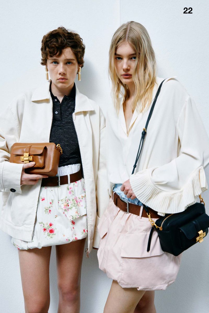 Two fashion models showcase designer handbags and clothing against a bright white backdrop in a studio setting, focusing on contemporary style.