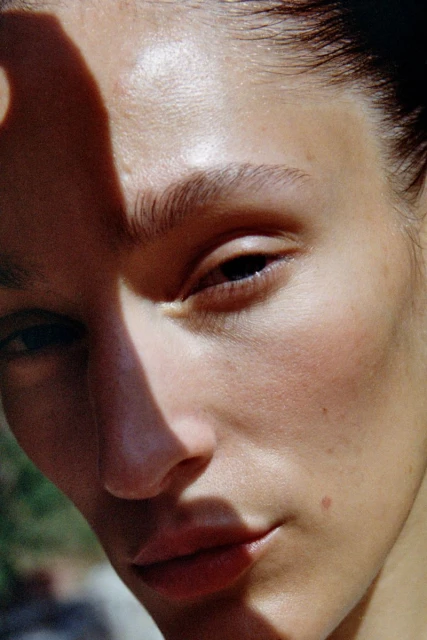 Close-up portrait of a young adult woman's face, with half her face shadowed, showcasing natural skin texture and minimalistic beauty look.