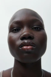Close up portrait of a bald Black model wearing glossy lip tint against a plain white background for Zara Beauty