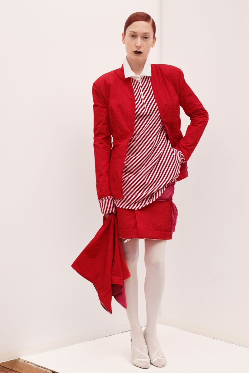Fashion model in red jacket and skirt with striped shirt poses in a white corner studio for a fashion editorial photoshoot.