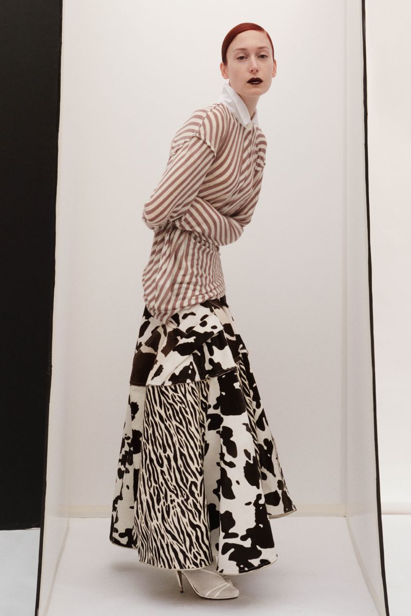 Fashion portrait of a red-haired model in a striped top and black-and-white print skirt posing in a white studio with a black accent.