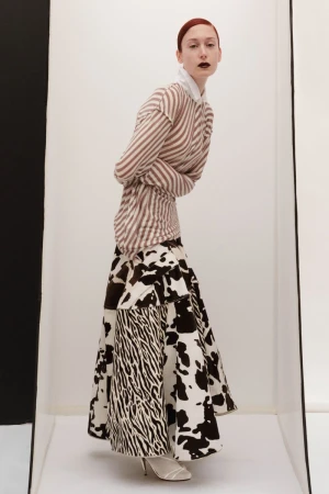 Fashion portrait of a red-haired model in a striped top and black-and-white print skirt posing in a white studio with a black accent.