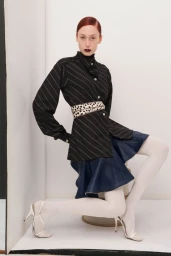 Model with red hair in a black pinstripe top and blue skirt posing against a white studio background for Talia Byre AW24.