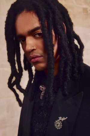 Model with long dreadlocks wearing a tailored black blazer with sparkling crystal brooches for Coach Resort 2025.