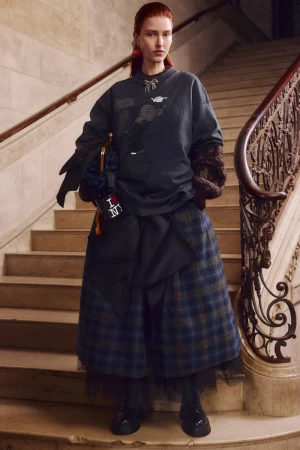 Fashionable redhead woman on marble stairs in a grey graphic sweatshirt, plaid skirt, accessorized with statement earrings and handbag.