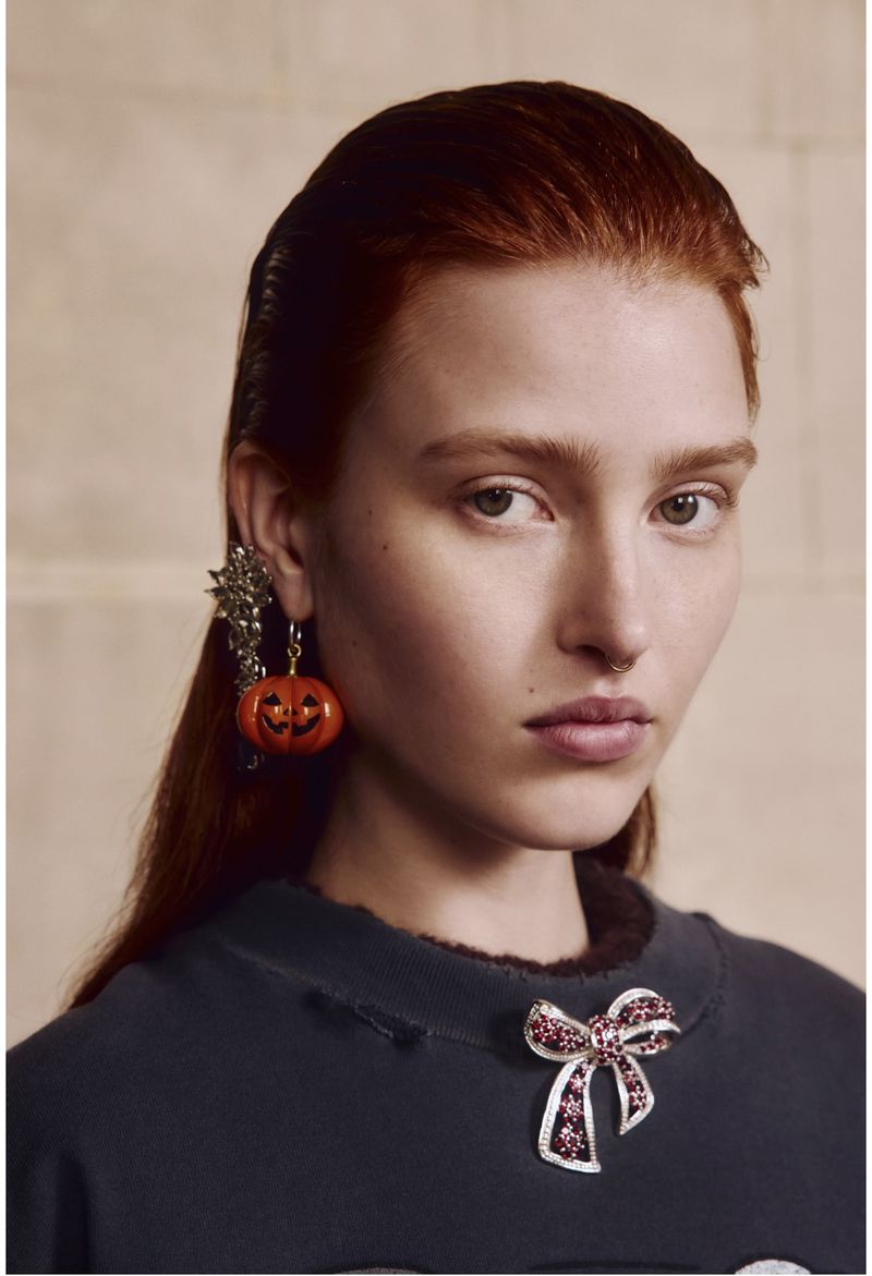 Close-up of a fair-skinned woman with red hair wearing pumpkin earrings and a bow brooch. Beauty shot for fashion or Halloween editorial.