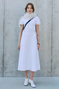 Model wearing a white dress and scarf standing against a concrete wall for 3.1 Phillip Lim Pre-Spring 2025