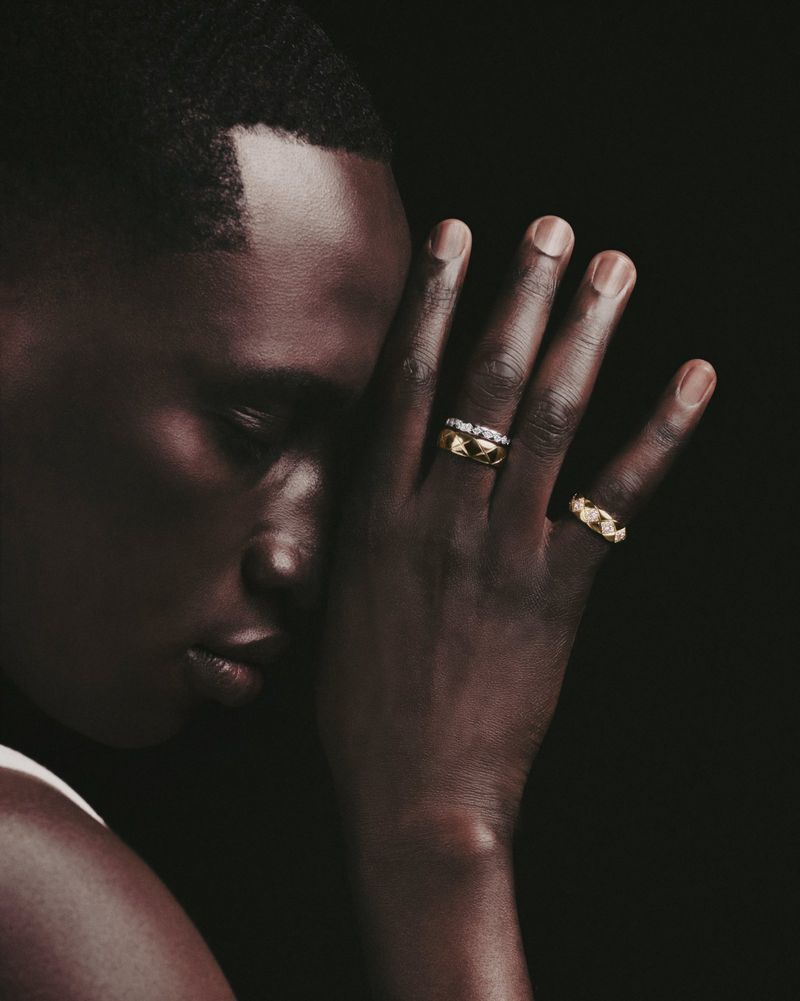 Close-up studio shot of a black man's hand adorned with gold rings. Dark backdrop enhances focus on the jewelry.