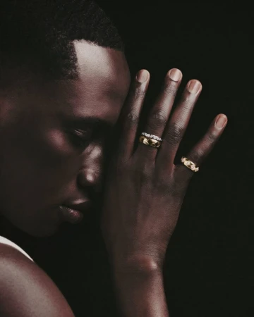 Close-up studio shot of a black man's hand adorned with gold rings. Dark backdrop enhances focus on the jewelry.