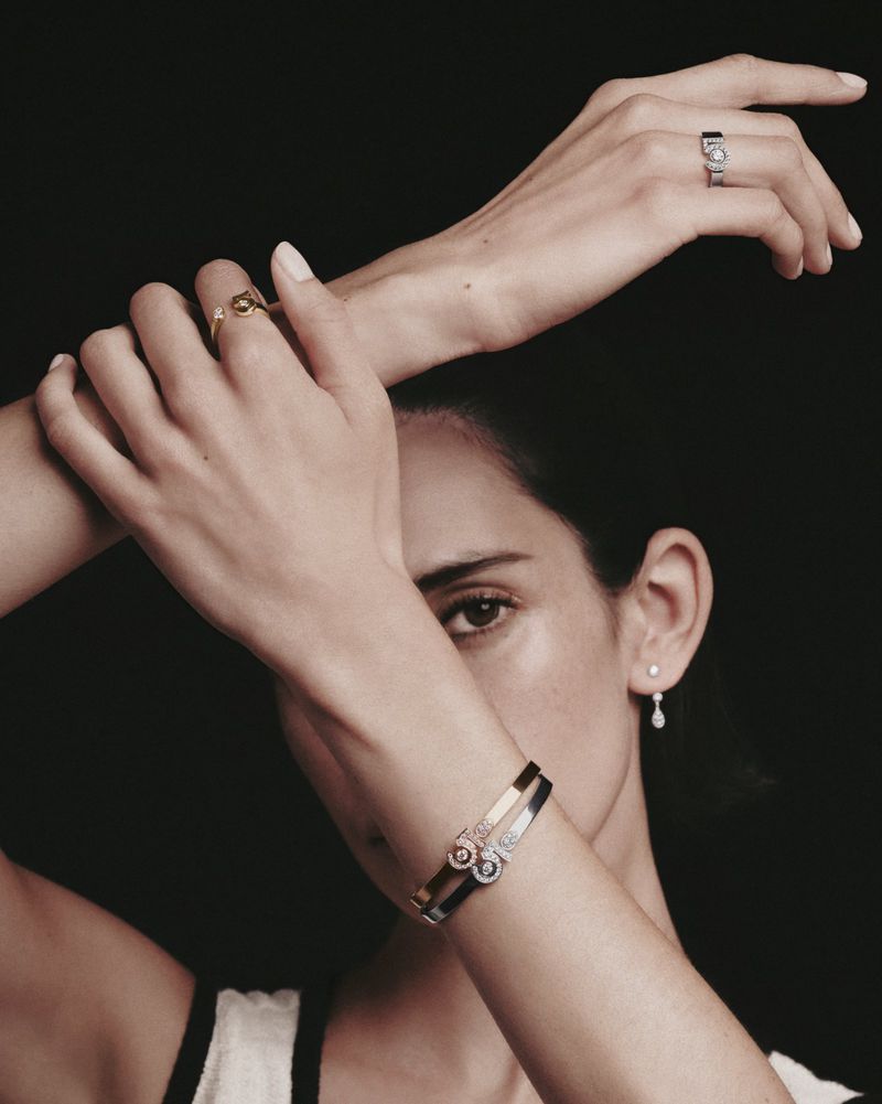 Close-up portrait of a woman wearing Chanel fine jewelry rings and bracelets against a dark background