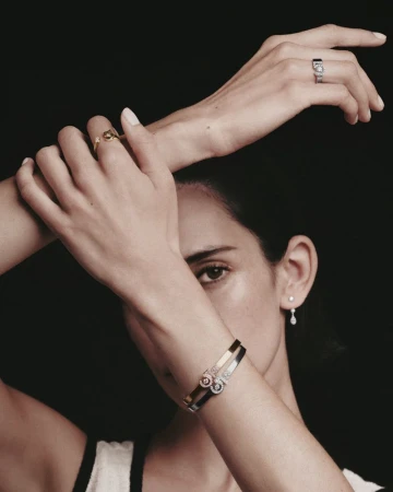 Close-up portrait of a woman wearing Chanel fine jewelry rings and bracelets against a dark background