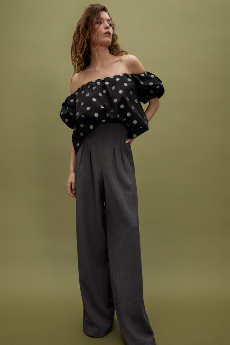 Fashionable woman posing in polka dot top and wide leg pants against green backdrop, studio lighting, promoting fashion apparel.