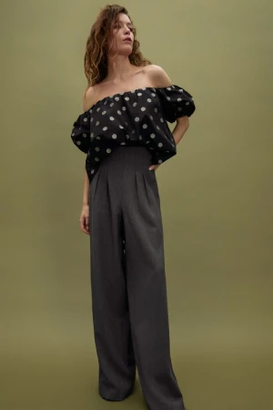 Fashionable woman posing in polka dot top and wide leg pants against green backdrop, studio lighting, promoting fashion apparel.