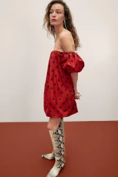 Model in red polka-dot off-the-shoulder dress and snakeskin boots against a neutral background
