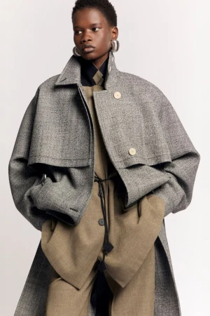 Model Mary Ukech wearing an oversized grey wool coat and beige trousers for the Lanvin Resort 2025 lookbook against a white backdrop.
