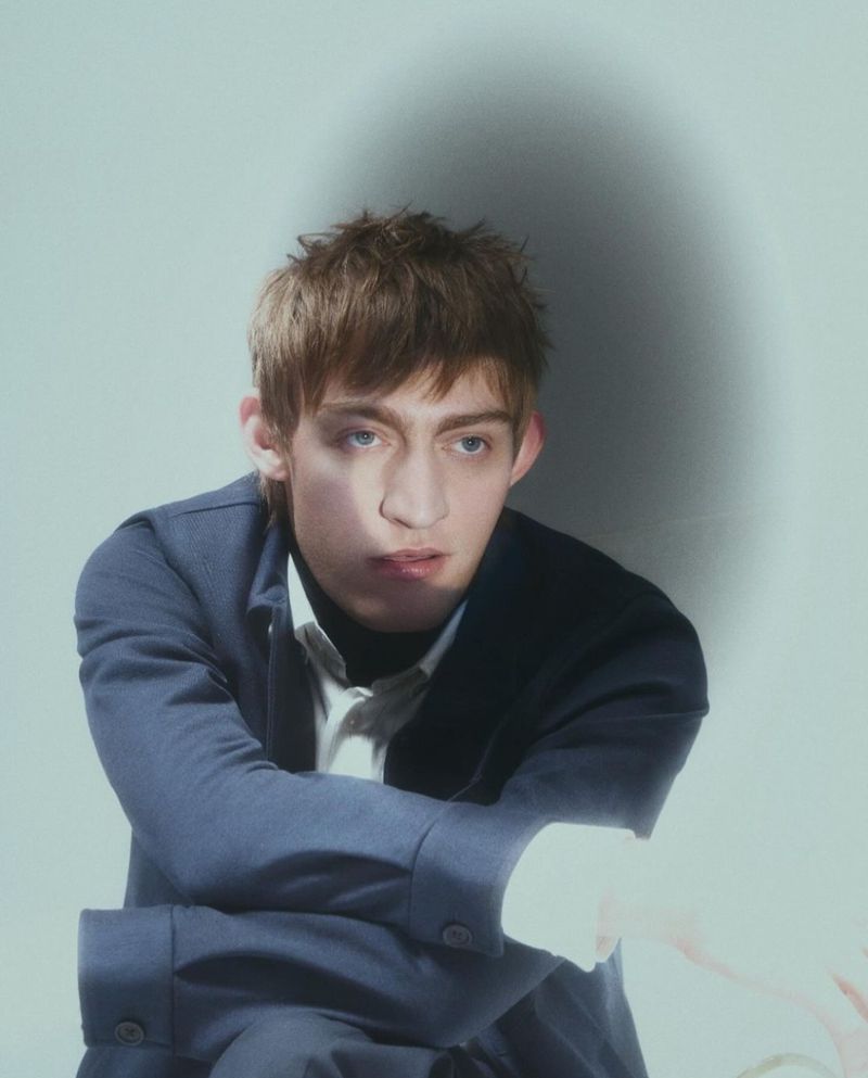 Model Dylan Moran posing in a navy blue jacket against a pale studio backdrop with soft shadow.