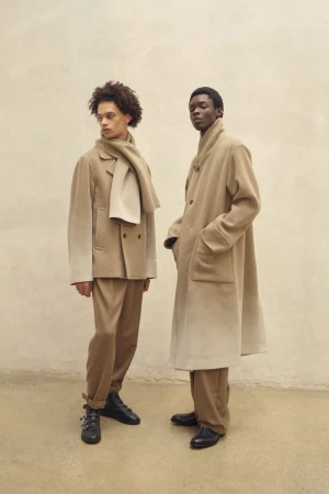 Two male models posing in coordinated beige wool coats, trousers, and black shoes against a neutral backdrop for IRENISA.