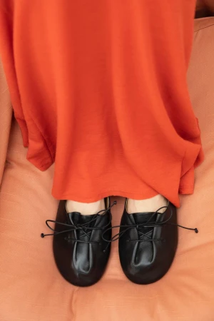 Top-down view of black gathered leather ballet flats paired with a vibrant draped orange skirt on a matching fabric background.