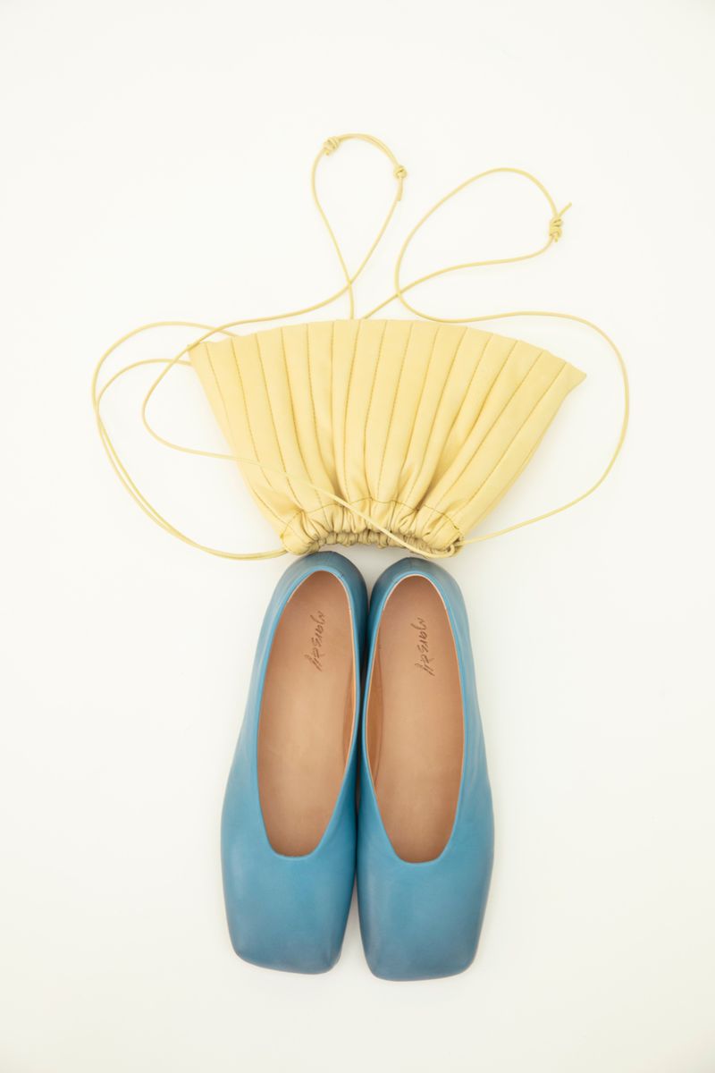 Flat lay of light yellow pleated purse with string straps paired with light blue square toe ballet flats on a solid white background.