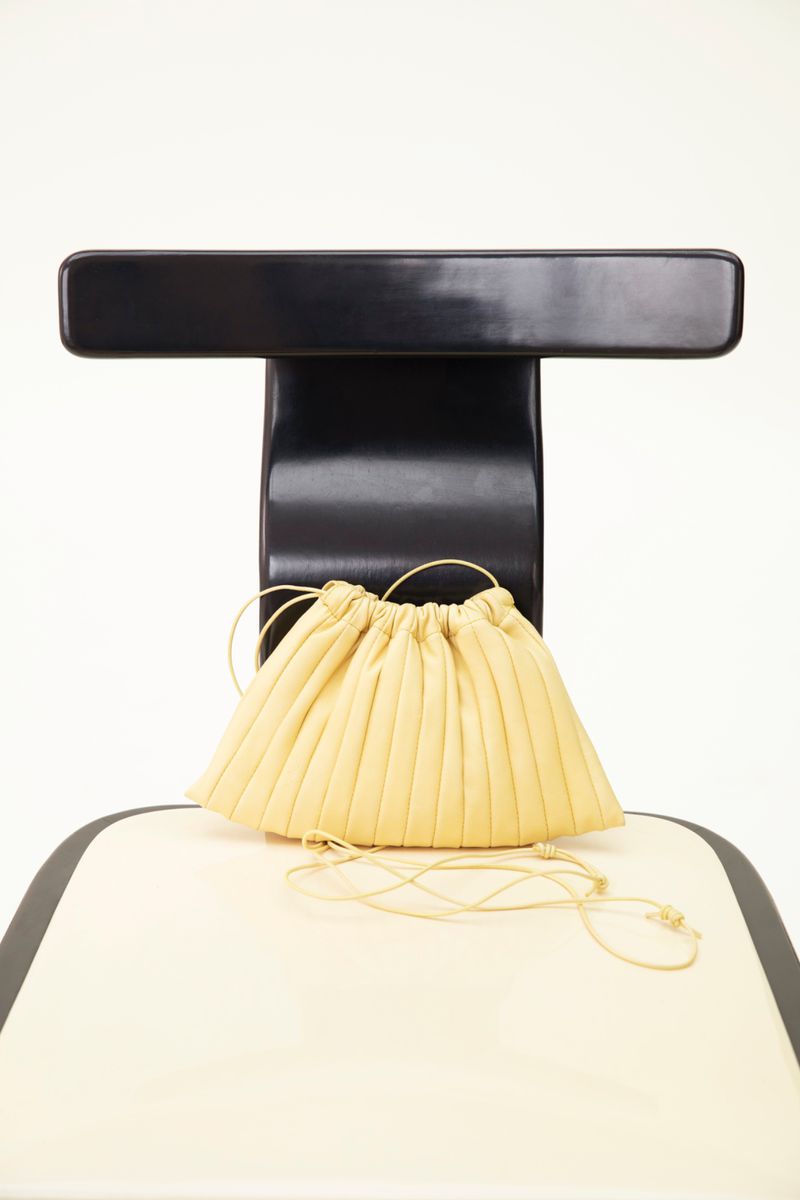 Pale yellow ruched drawstring purse bag on a black and cream chair against a white backdrop, studio lighting, close-up.