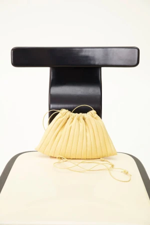 Pale yellow ruched drawstring purse bag on a black and cream chair against a white backdrop, studio lighting, close-up.