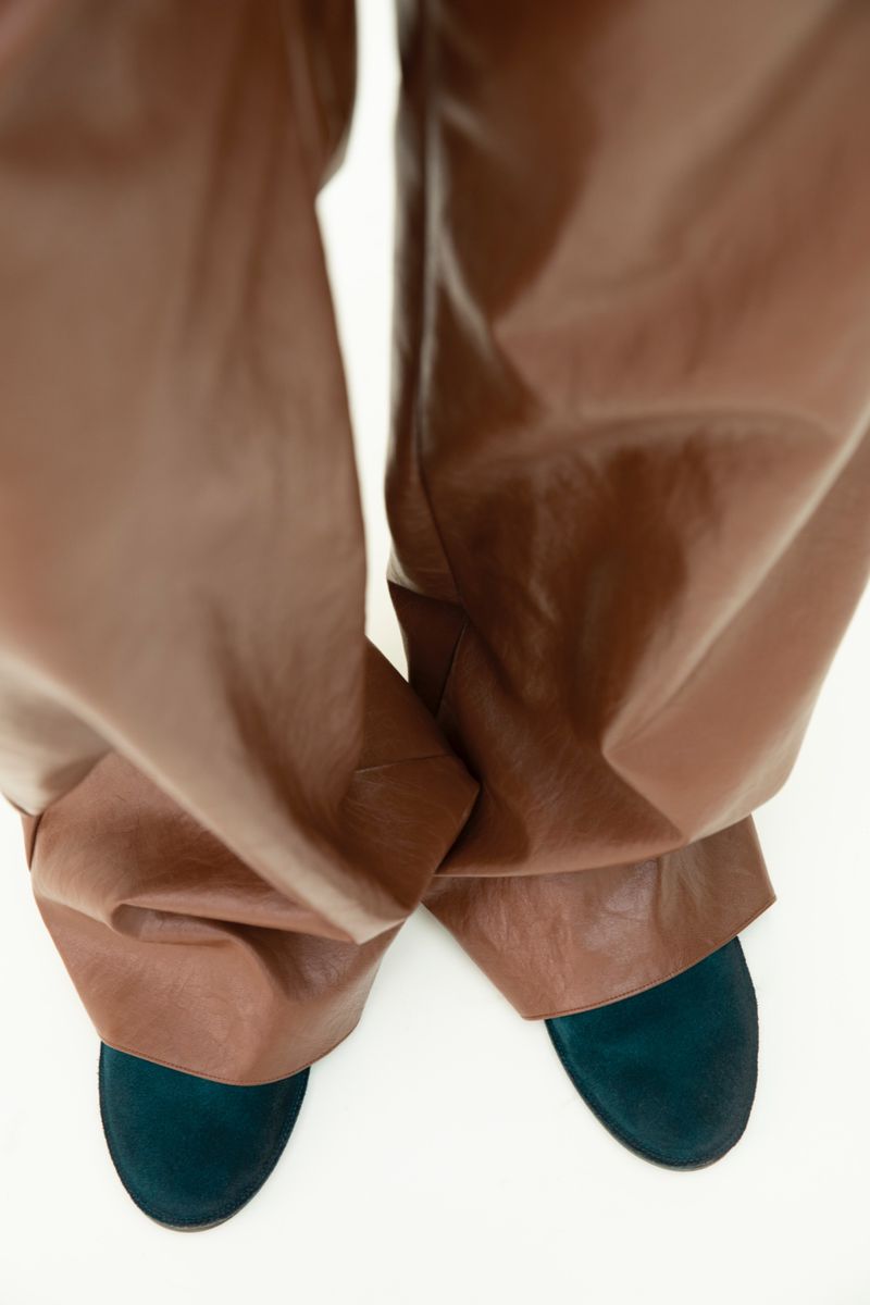 Eye-level shot showcasing brown leather pants paired with blue suede shoes, set against a stark white background.