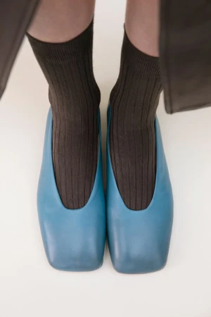 A close-up of blue leather ballet flats worn with ribbed brown socks, set against a plain white background.