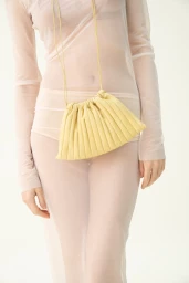 Model wearing sheer white mesh dress holding a gathered yellow leather handbag for Marsèll ss24