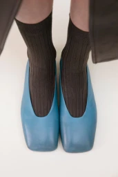 Close-up overhead shot of feet wearing blue leather shoes and ribbed brown socks on a neutral background.