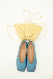 Blue leather flats and yellow gathered pouch bag arranged on a bright white studio background.