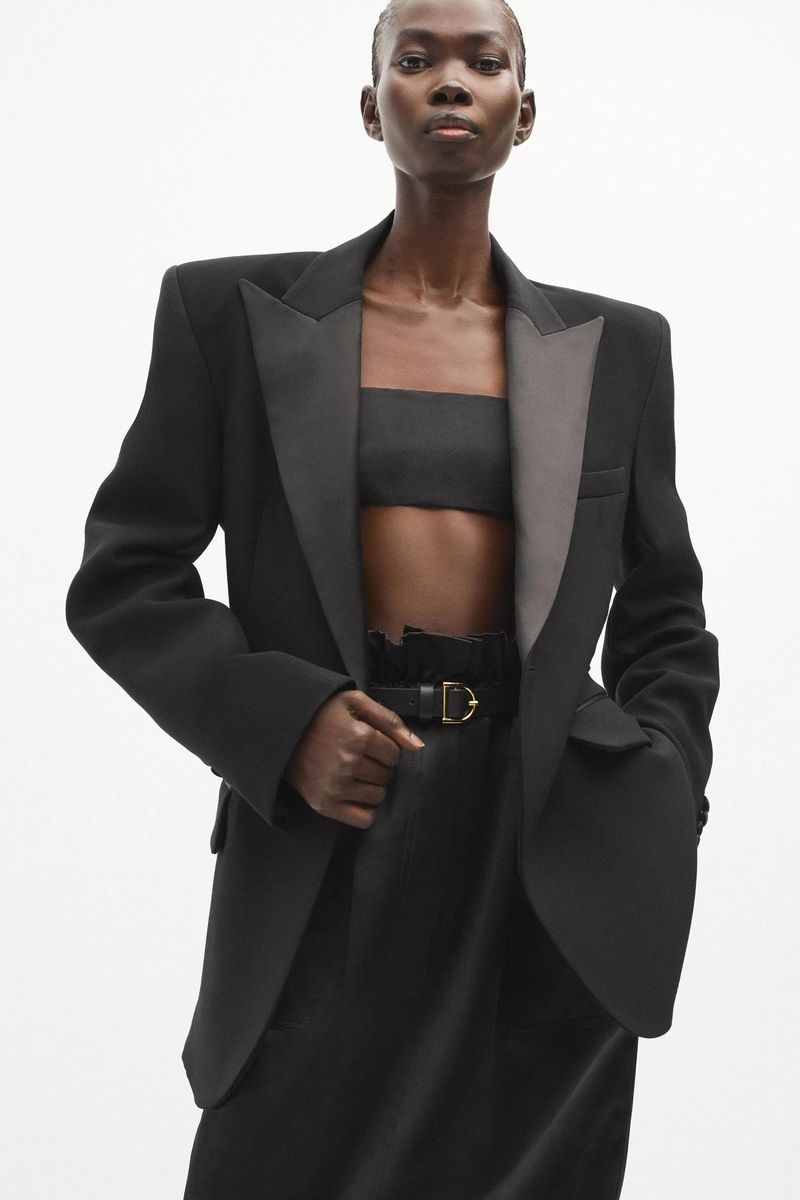 Elegant black woman in a tailored blazer and bandeau top, posing against a bright background in a fashion forward, studio shot.