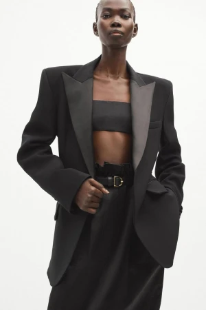 Elegant black woman in a tailored blazer and bandeau top, posing against a bright background in a fashion forward, studio shot.