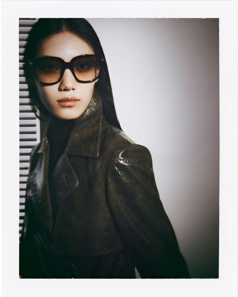 Portrait of an Asian woman with long black hair wearing sunglasses and a snakeskin jacket in a photo studio setting.