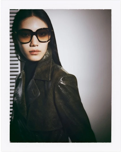 Portrait of an Asian woman with long black hair wearing sunglasses and a snakeskin jacket in a photo studio setting.