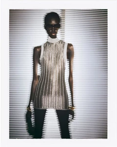 Model in dark sunglasses and metallic top standing against horizontal blinds for Tom Ford Women's Wear Fall 2024 campaign.