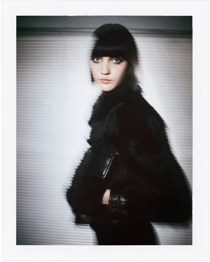 Model with dark bob hairstyle wearing a black textured jacket against a horizontal slat blind background
