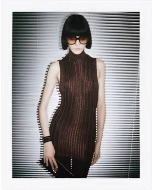 Model in brown sleeveless top and oversized sunglasses posing in front of horizontal window blinds