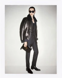 Model Meng Yu Qi in a black leather shearling jacket, dark tailored suit, sunglasses, and leather clutch bag for Tom Ford Men's Fall 2024.