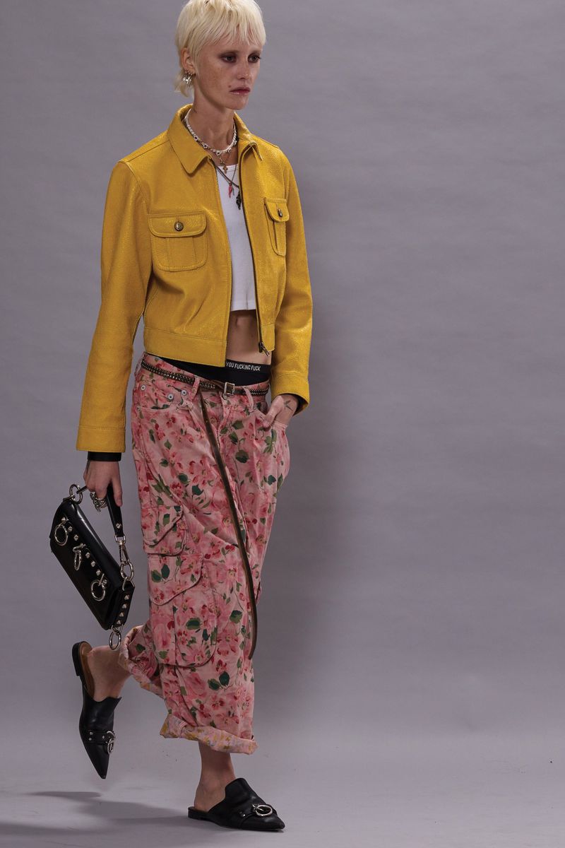 A woman models a yellow jacket and pink floral pants with black accessories. She is posing in a fashion forward style.