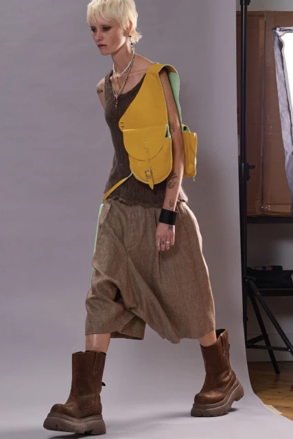 Fashion photo of a person with a yellow crossbody bag, wearing a brown top and skirt, posing in a studio with a light stand.