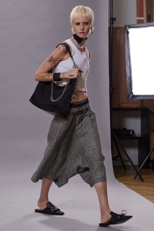 Model with short blonde hair walks in a white tank top, wide-leg cropped grey culottes, and black pointed mules carrying a shoulder bag.