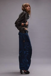 Model in a black leather jacket and blue trousers posing against a grey background for R13 Resort 24.